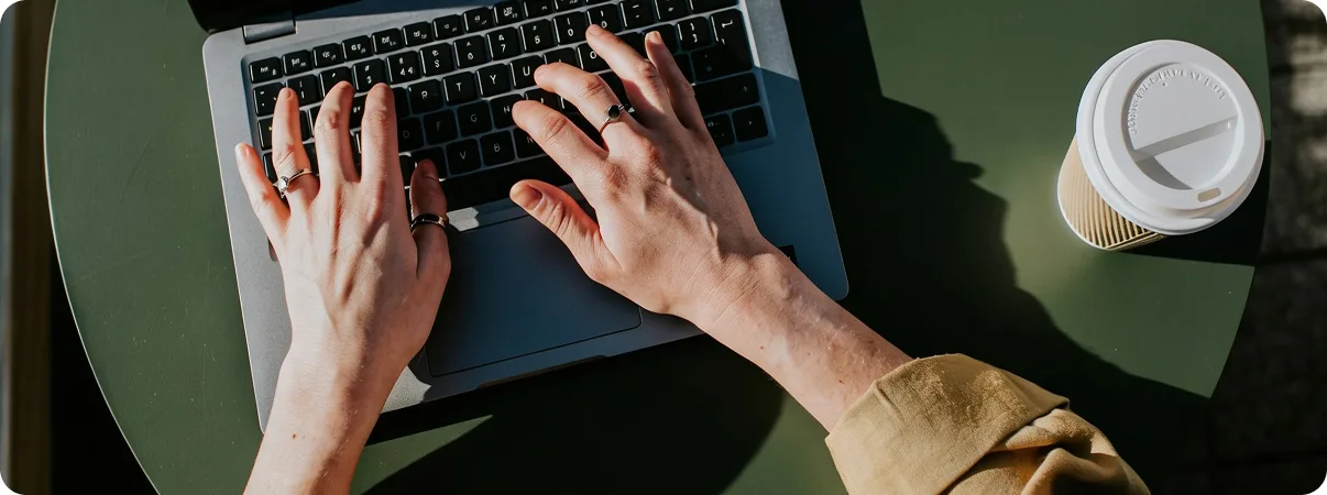 Mani al lavoro su un laptop accanto a una tazza di caffè